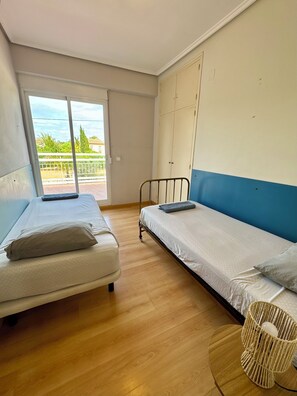 A room with two beds, a large window, and a view of greenery outside.
