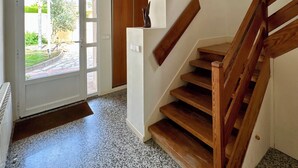 Eine Treppe mit Holzstufen und Geländer, die zu einem Innenraum mit einer weißen Tür und Blick ins Freie führt.