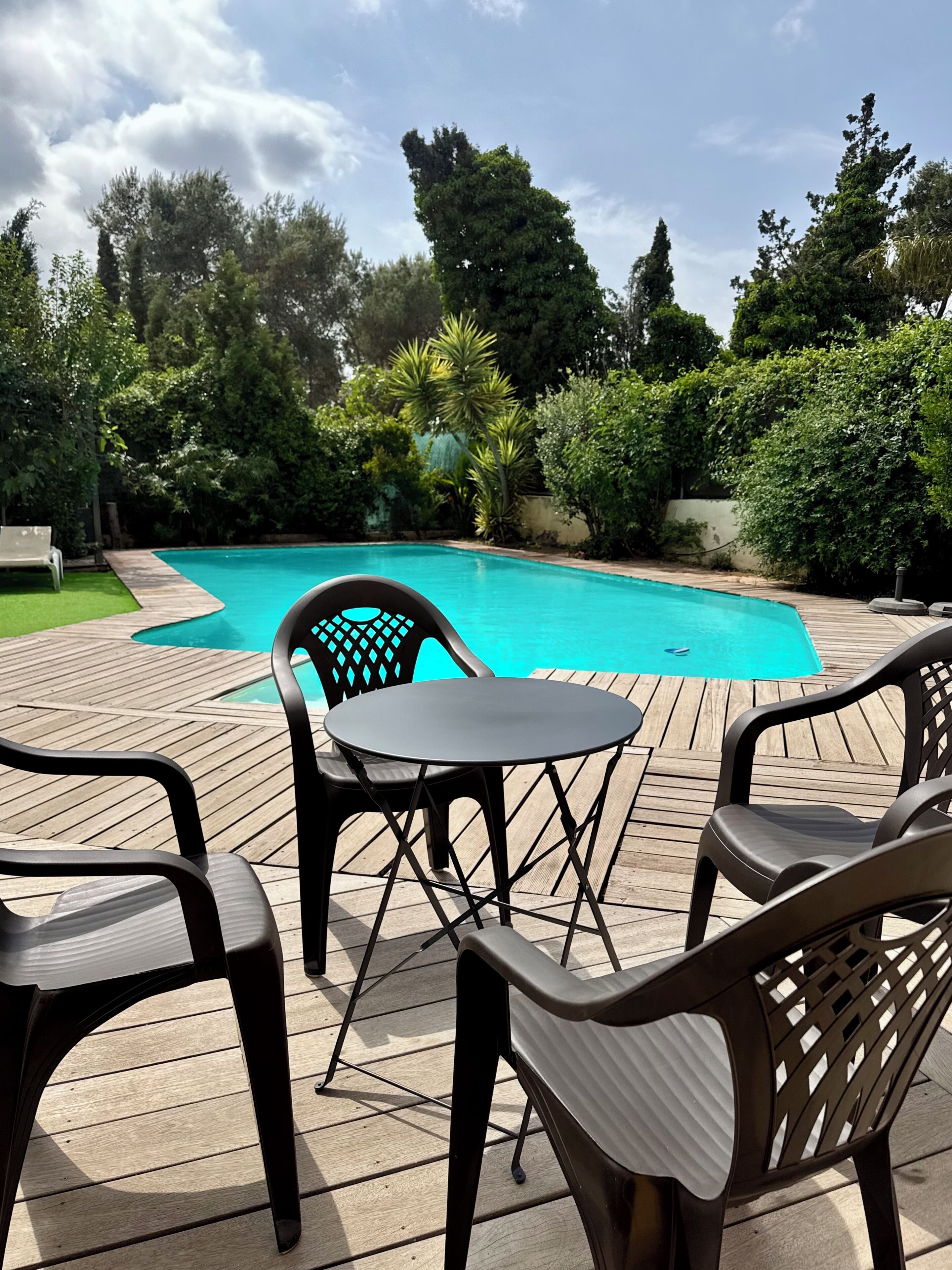Un área de piscina al aire libre con cubierta de madera, rodeada de follaje y árboles.