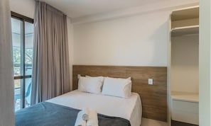 Hotellihuone, jossa on sänky, puinen pääty, ikkuna verhoilla ja sisäänrakennettu vaatekaappi.