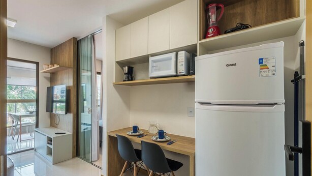 A modern kitchen with a refrigerator, microwave, and coffee maker. There is a dining area with a table and chairs. - Apt w/ Balcony 290 m From the Beach Hoa0308 (Salvador)