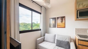 Quarto com uma janela ampla, um sofá branco, duas quadros na parede e uma TV de tela plana.