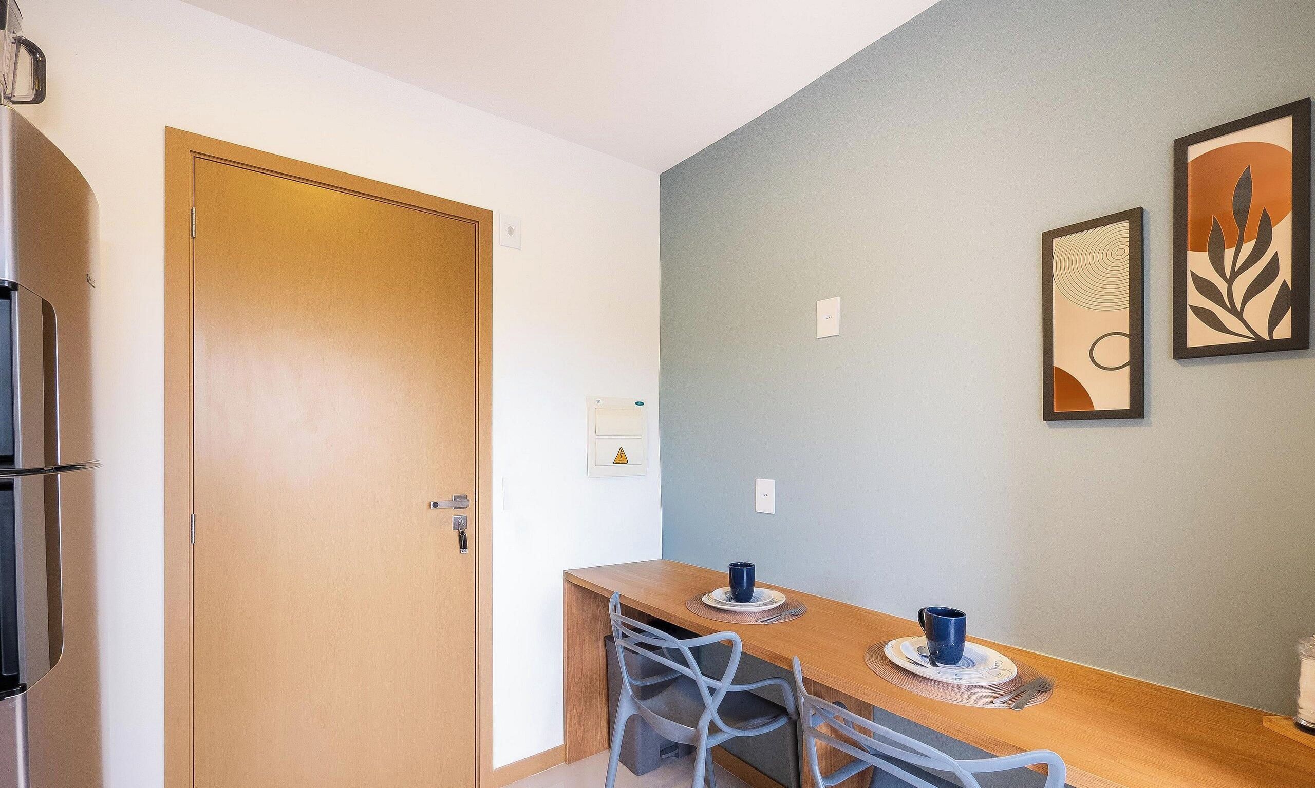 Una cocina compacta con puerta de madera, una mesa de comedor con sillas y dos cuadros en la pared.