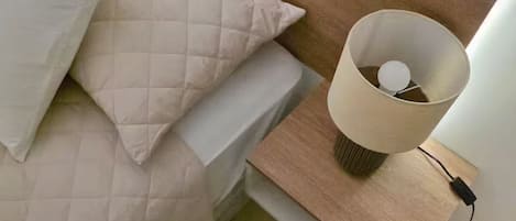 A bed with a headboard, pillows, and a bedside table with a lamp and charger.