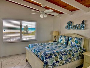 A bedroom with a bed, a ceiling fan, a window with blinds, and a wall decoration. - Gulf-front 2BR Siesta Key condo with beach views. (Siesta Key)