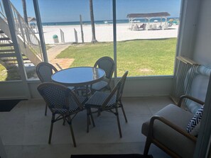 Ein Balkon mit Tisch und Stühlen, der Blick auf einen Strand mit Kiosk und Liegestühlen freigibt.