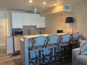 A compact kitchen with white cabinets, a microwave, a sink, and a ceiling fan. - Gulf-front 1BR Siesta Key condo with king bed and sleeper sofa. (Siesta Key)