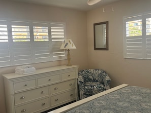 A bedroom with a bed, a dresser with drawers, a chair, a lamp, and a window with blinds. - Gulf-front 1BR Siesta Key condo with king bed and sleeper sofa. (Siesta Key)