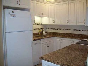 A kitchen with white cabinets, a granite countertop, and a white refrigerator. - Gulf-front 1BR Siesta Key escape with king bed and sleeper sofa. (Siesta Key)