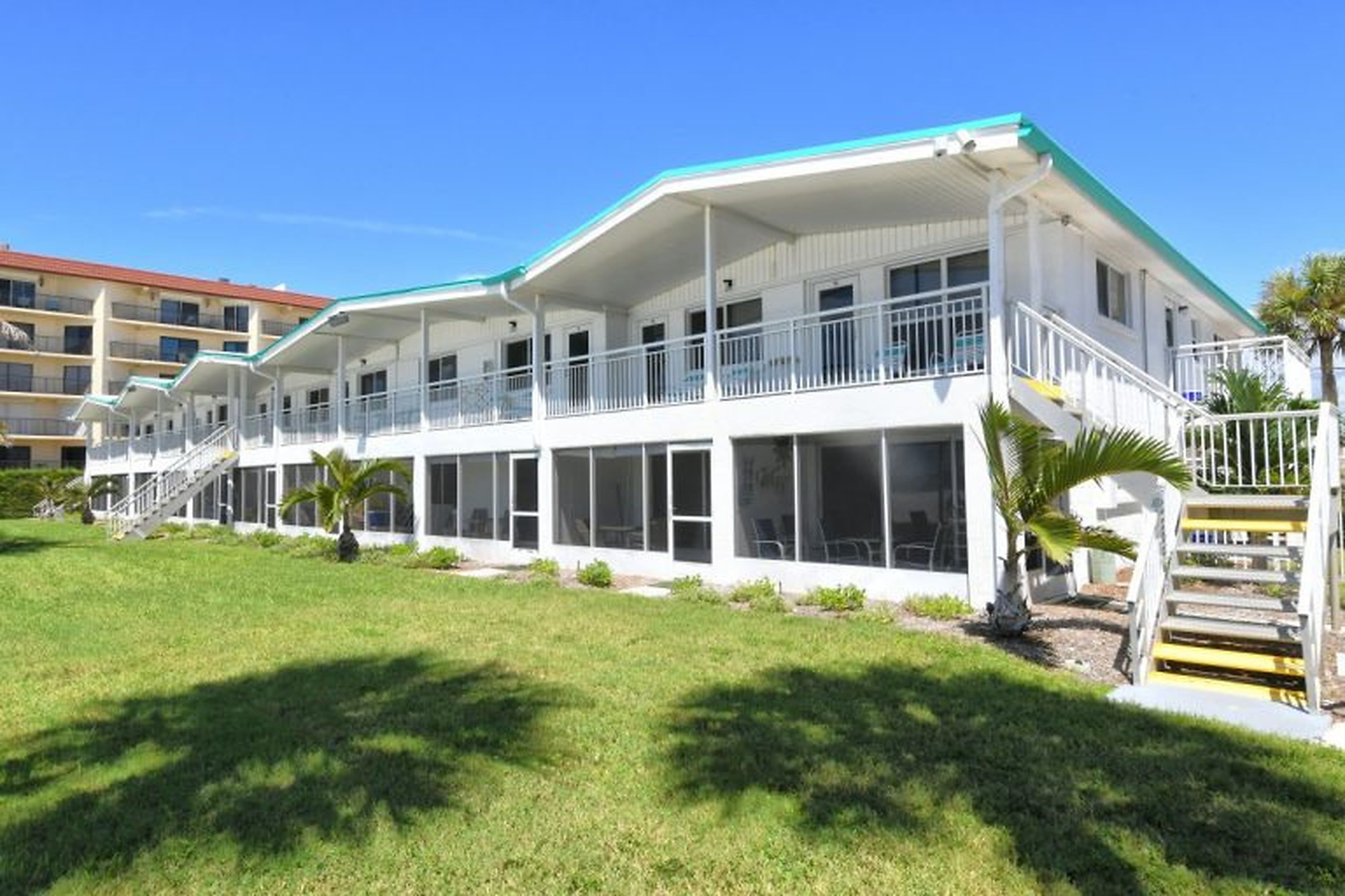 Un hotel de varios pisos con balcones, un área exterior techada y un césped.