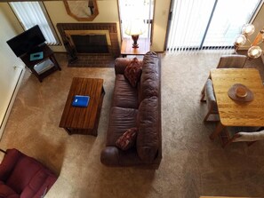 A living room with a brown leather sofa, a wooden coffee table, a red armchair, a fireplace, and a dining table with a lamp.