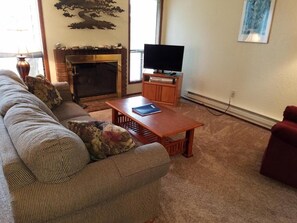 A living room with a sofa, a coffee table, a fireplace, and a television. - Amazing 2-bedroom condo with loft in soothing Port Townsend getaway (Port Townsend)