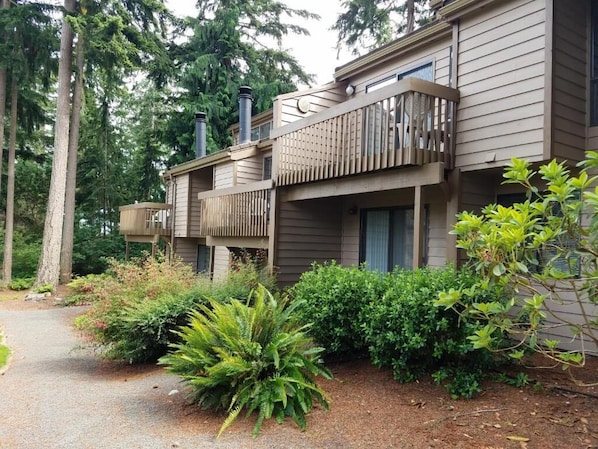 A two-story building with a balcony, surrounded by dense greenery and trees.