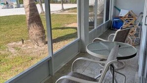 A covered outdoor seating area with a glass table and chairs, a view of palm trees, and a clear sky. - SR-12A Gulf Front 1/1 (Siesta Key)