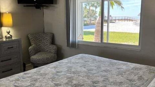 A bedroom with a bed, a television, a chair, a window with a view of the beach, and a ceiling fan. - SR-12A Gulf Front 1/1 (Siesta Key)
