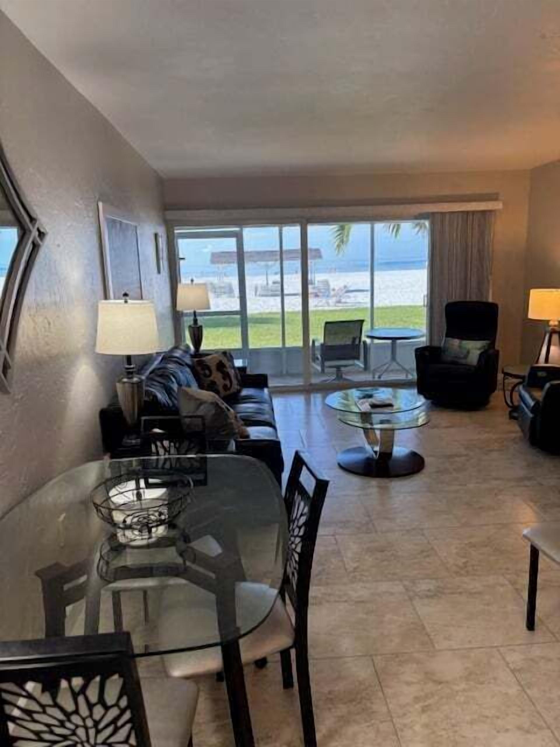 Habitación de hotel con una mesa de vidrio, un sofá, una silla y vista a la playa.