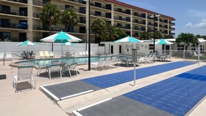 A hotel pool area with lounge chairs and umbrellas, a pool, and a multi-story building in the background. - SR-12A Gulf Front 1/1 (Siesta Key)