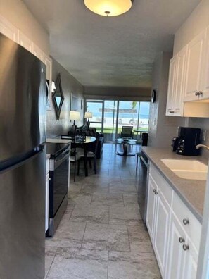 A kitchen with a refrigerator, stove, and sink, with a view of the outdoors. - SR-12A Gulf Front 1/1 (Siesta Key)