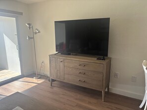 A room with a wooden cabinet, a flat-screen TV, and a floor lamp. - SR-15 Ground Floor Gulf Front (Siesta Key)