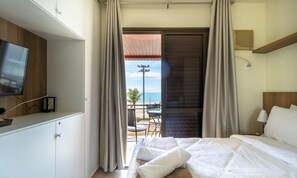 Une chambre d’hôtel avec un lit, une télévision, un balcon avec une table et des chaises, et une vue sur la mer.