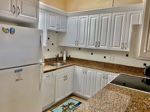 A kitchen with white cabinets, a granite countertop, and a stainless steel sink. - SR-16 Eclectic 2nd Floor Gulf Front (Siesta Key)