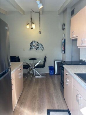A compact kitchen with modern appliances, a dining area with a glass table, and a hanging light fixture. - SR-18 - 2nd Floor Gulf Front (Siesta Key)