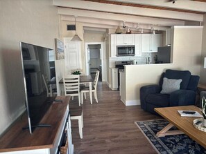 Ein modernes Wohnzimmer mit einem Flachbildfernseher, einem dunkelgrauen Sofa mit dekorativem Kissen und einem Holztisch.