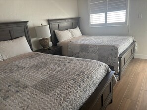 A bedroom with two beds, a nightstand with a lamp, and a window with blinds. - SR-20 - 1/1 Close to Pool (Siesta Key)