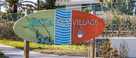 Un letrero para Sierra Key Village, con un diseño natural en un lado y un edificio moderno al fondo.