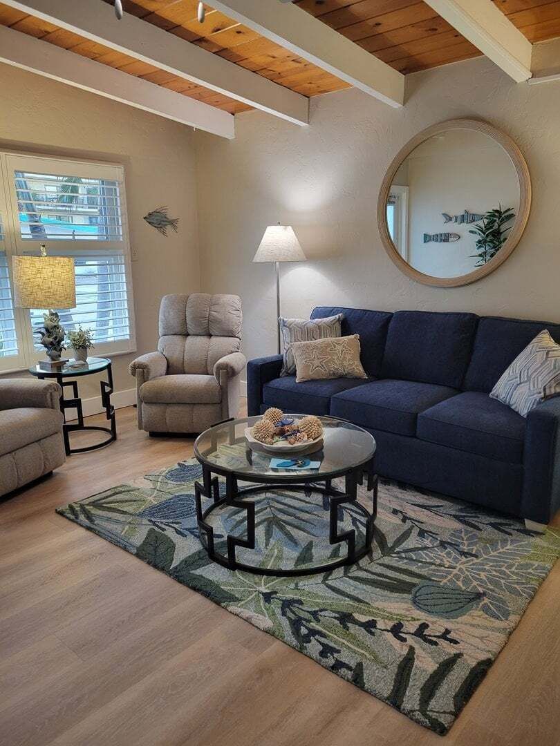 Un salon avec un canapé bleu, un fauteuil beige, une table basse ronde et un tapis à motifs.