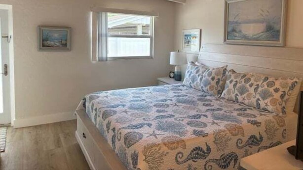 A bedroom with a bed, a ceiling fan, a window, and a painting on the wall. - SR-23 Lovely 1/1 Unit (Siesta Key)