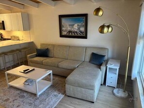A living room with a sofa, a coffee table, a floor lamp, and a painting on the wall. - SR-23 Lovely 1/1 Unit (Siesta Key)