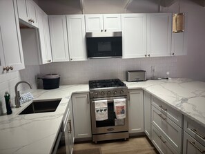 A modern kitchen with white cabinets, a stainless steel stove, a microwave, and a toaster. - SR-23 Lovely 1/1 Unit (Siesta Key)