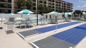 A hotel pool area with sun loungers, umbrellas, and a building with balconies in the background. - SR-23 Lovely 1/1 Unit (Siesta Key)