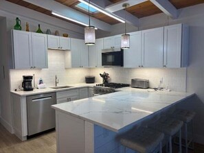 A modern kitchen with white cabinetry, a large island, and bar stools. - SR-23 Lovely 1/1 Unit (Siesta Key)