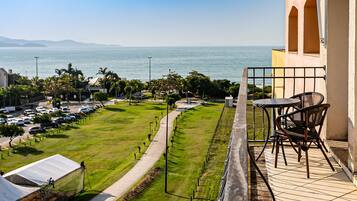 Uma varanda com vista para o mar, área gramada e carros estacionados.