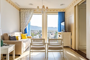 Ein Wohnzimmer mit einer Couch, zwei Sesseln, einem Fernseher und Bergblick durch große Fenster.