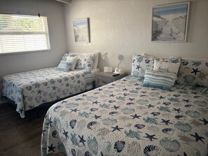 Ein Schlafzimmer mit zwei Betten, jeweils mit einem marineblauen Bettbezug, einem Nachttisch mit Lampe und einem gerahmten Bild an der Wand.