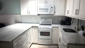 A kitchen with white cabinets, a microwave, a stove, and a coffee maker. - SR- North Court Unit (Siesta Key)