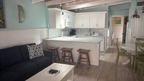 A modern kitchen with white cabinets, a central island, and wooden stools. - SR- North Court Unit (Siesta Key)
