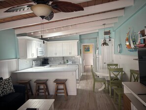 A kitchen with white cabinets, a central island, and a dining area with green chairs. - SR- North Court Unit (Siesta Key)