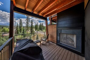 A wooden deck with a fireplace, outdoor seating, and a view of a forest and mountains. - Hot Tub | Mountain Views | Walk To Downtown (Winter Park)