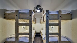 Ein Schlafraum mit Etagenbetten und einem zentralen Gang, ausgestattet mit Holzbettstühlen und einem Deckenventilator.