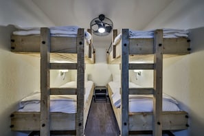 Ein Schlafraum mit Etagenbetten und einem zentralen Gang, ausgestattet mit Holzbettstühlen und einem Deckenventilator.
