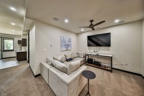 A modern living room with a sectional sofa, a coffee table, a TV mounted on the wall, and a ceiling fan. - Hot Tub | Mountain Views | Walk To Downtown (Winter Park)