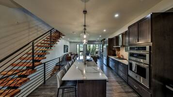 A modern kitchen with a central island, dark cabinetry, stainless steel appliances, and a staircase with wooden steps.