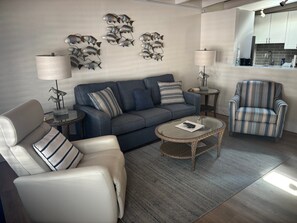 Ein modernes Wohnzimmer mit Sofa, Sessel und Couchtisch. Im Hintergrund ist eine Küchenzeile erkennbar.