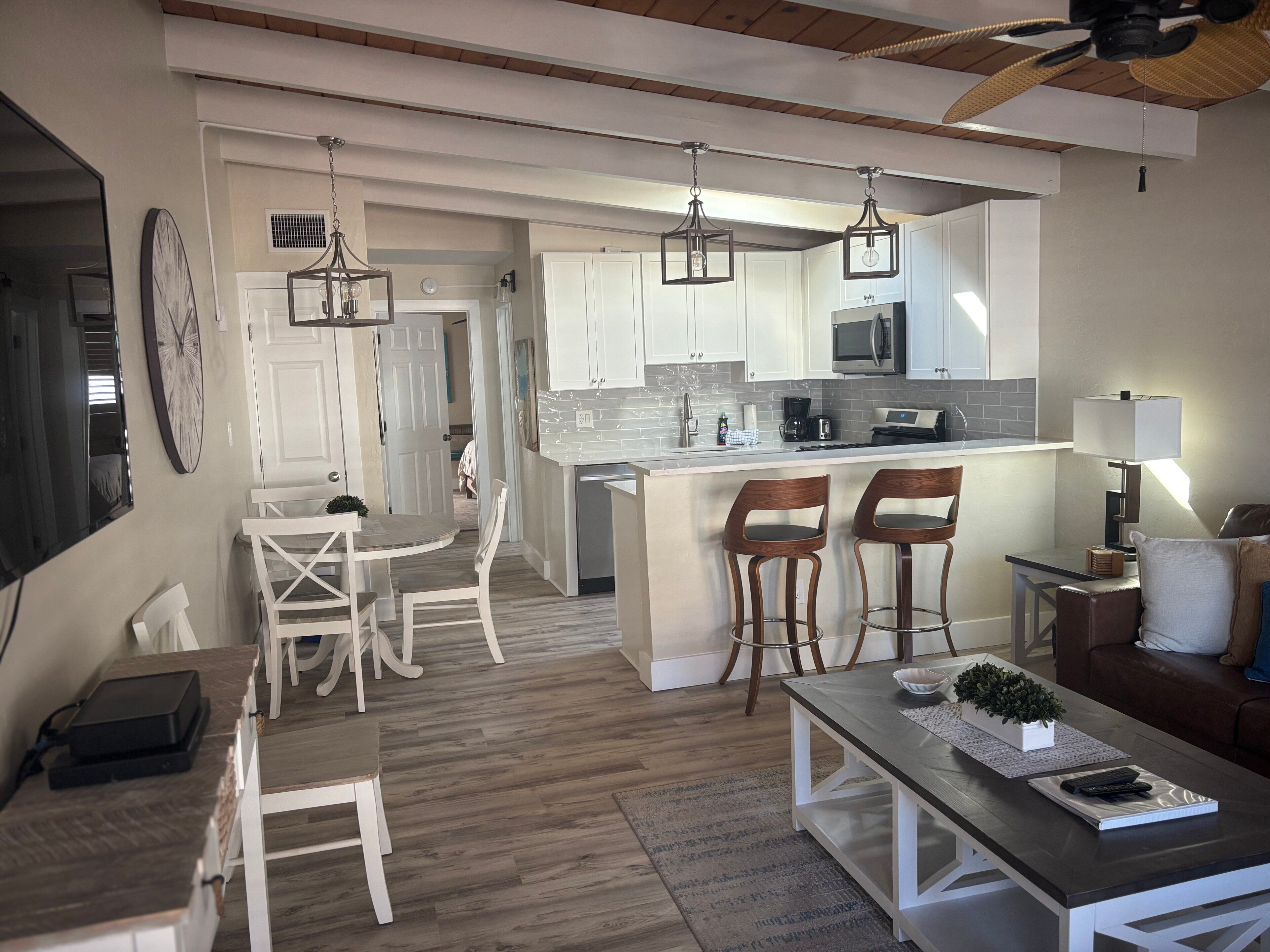Une cuisine moderne avec des meubles blancs, un îlot central doté de tabourets et des luminaires suspendus.