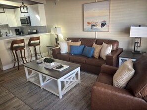 Ein Wohnzimmer mit braunem Ledersofa, einem Couchtisch und einer Küche im Hintergrund.