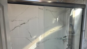 Une salle de bain moderne avec une douche à parois de verre, des toilettes et un mur recouvert de carreaux de marbre.